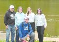 Aaron Houser kneels beside Coalbie, a therapy dog wearing a pink vest, as four supporters stand behind them along the Monongahela River in Greensboro, Pennsylvania.