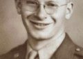 A smiling young World War II U.S. Army soldier wearing glasses, a military uniform, and a service cap poses for a vintage sepia-toned portrait.