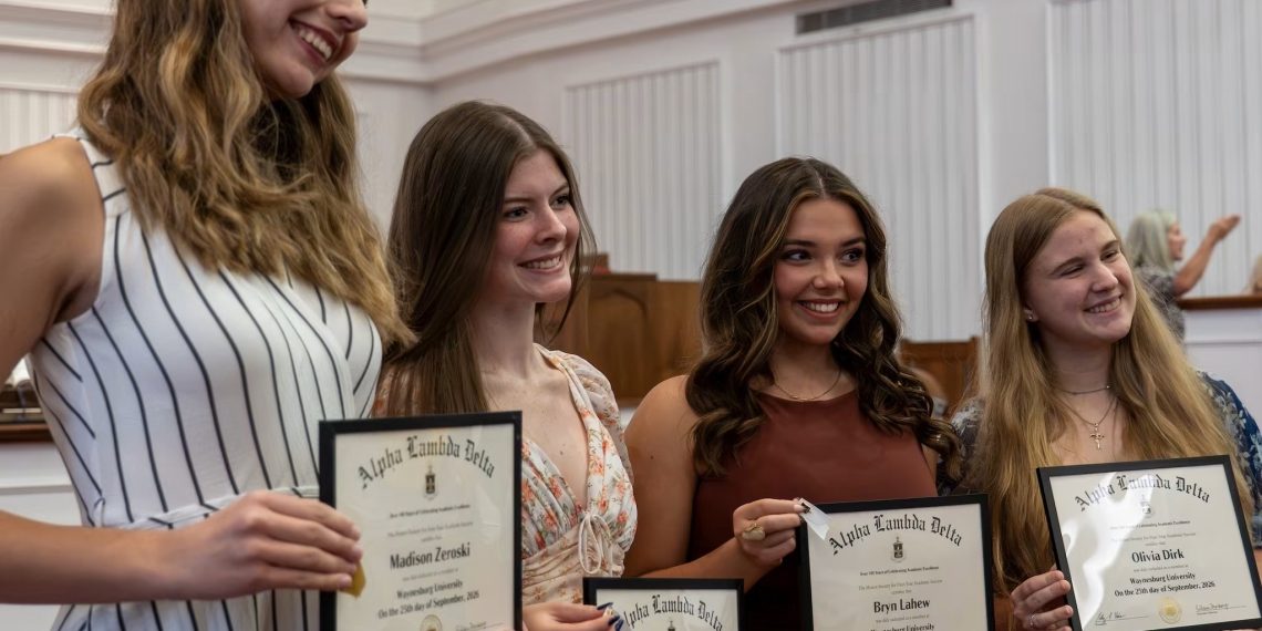 Four smiling Waynesburg University students pose together while holding framed Alpha Lambda Delta honor society certificates.