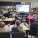 Jefferson-Morgan Elementary GATE students listen to a presenter holding a magazine page beside a screen displaying Backroads Magazine in their school library.