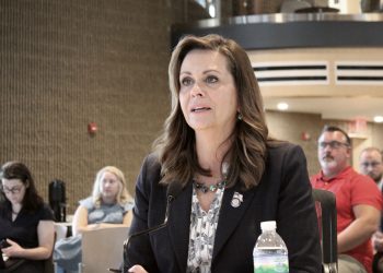 Pennsylvania State Senator Camera Bartolotta, wearing a dark blazer and patterned blouse, speaks into a microphone during a public hearing with attendees in the background.