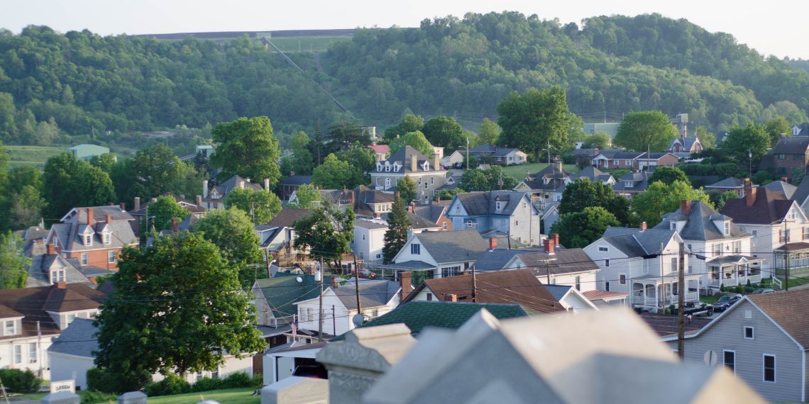 A panoramic view of Waynesburg, Pennsylvania, featuring residential homes, lush green hills, and cemetery headstones in the foreground.