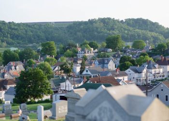 A panoramic view of Waynesburg, Pennsylvania, featuring residential homes, lush green hills, and cemetery headstones in the foreground.