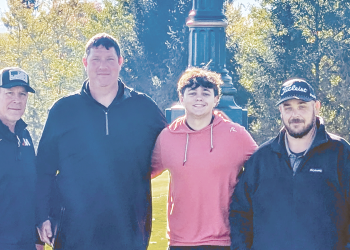 Jefferson-Morgan senior golfer Miles Sowden stands with three supporters beneath the large Oakmont Country Club Rolex clock on a sunny day.