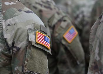 Close-up of U.S. military personnel wearing camouflage uniforms with embroidered American flag patches on their sleeves.