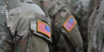 Close-up of U.S. military personnel wearing camouflage uniforms with embroidered American flag patches on their sleeves.