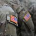 Close-up of U.S. military personnel wearing camouflage uniforms with embroidered American flag patches on their sleeves.